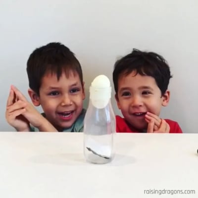 Hava basıncıyla şişeye çekilen sert haşlanmış yumurtaya bakan iki çocuk