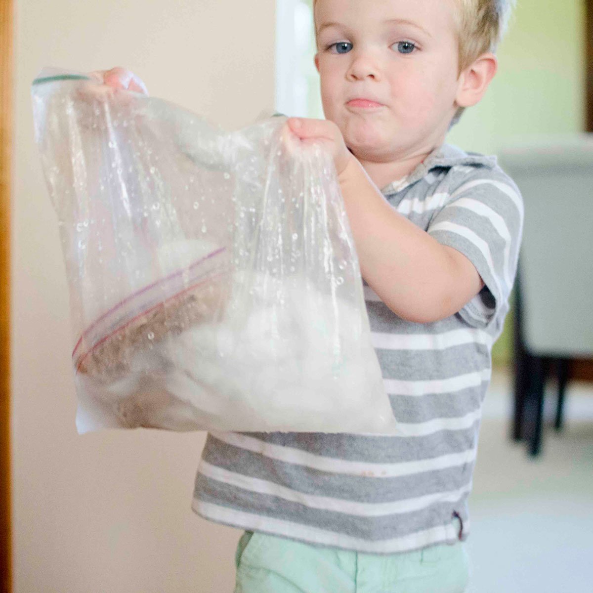 Yeni yürümeye başlayan bir çocuk plastik bir torba tutar. Çantada dondurma yapmak için sallıyor.